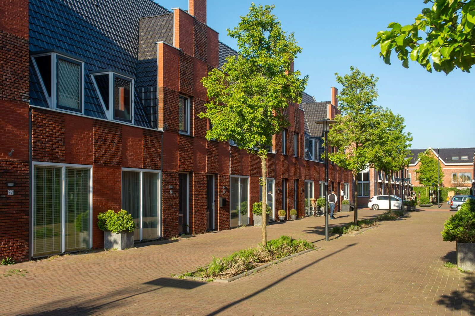 A bright suburban street lined with modern brick row houses and lush greenery, capturing a peaceful urban neighborhood vibe.
