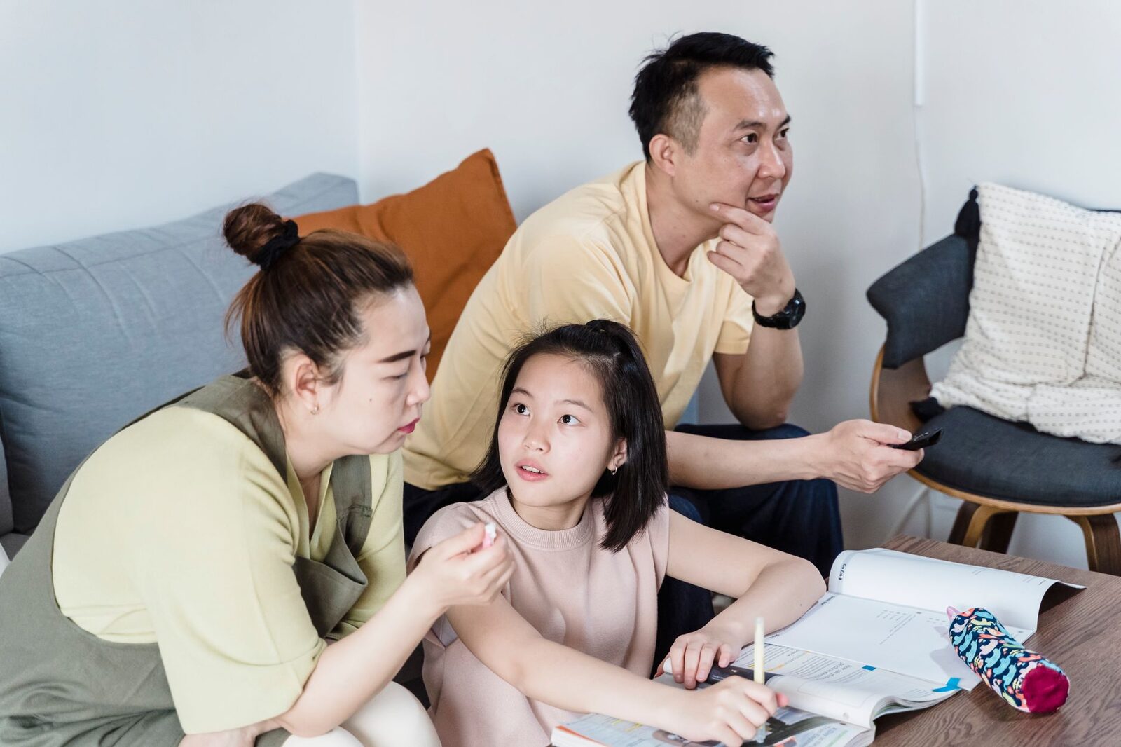 Parents helping daughter with homework in a cozy living room setting.